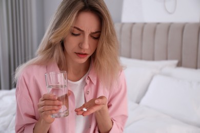 Upset young woman with abortion pill and glass of water at home
