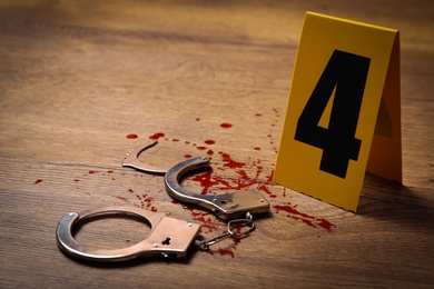 Photo of Handcuffs with blood and crime scene marker on wooden table, closeup