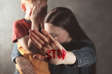 Photo of Scared little boy and mother with word Stop written on hand against light grey background, closeup. Domestic violence concept