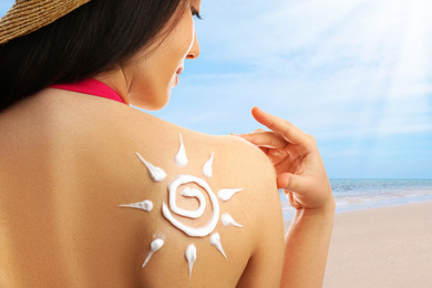 Young woman with sun protection cream on her back at beach, closeup