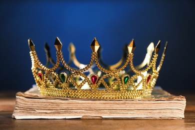 Beautiful golden crown on old book against dark blue background. Fantasy item