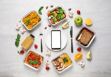 Flat lay composition with lunchboxes and smartphone on white wooden table, mockup for design. Healthy food delivery