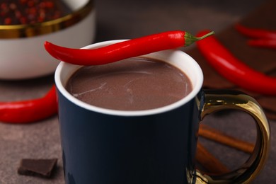 Photo of Cup of hot chocolate with chili pepper on grey table, closeup