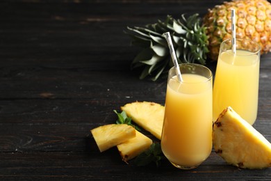 Photo of Delicious pineapple juice and fresh fruit on black wooden table. Space for text