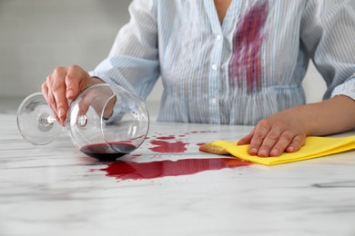 Woman with stain on her shirt cleaning spilled wine from white marble table indoors, closeup