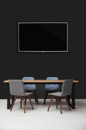 Modern wide screen TV on black wall in room with stylish furniture 