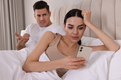 Internet addiction. Woman with smartphone ignoring her boyfriend in bedroom