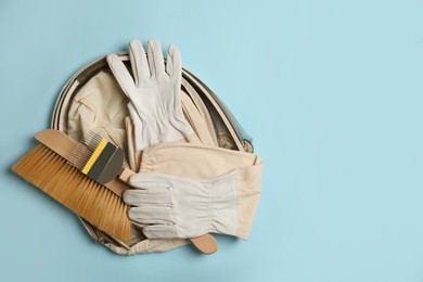 Beekeeping tools and uniform on light blue background, top view. Space for text