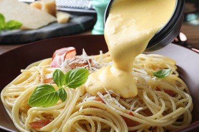 Pouring tasty cheese sauce onto spaghetti with meat, closeup