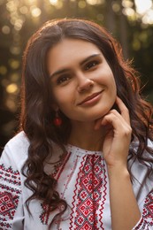 Photo of Beautiful woman in embroidered shirt outdoors on sunny day. Ukrainian national clothes