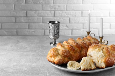 Homemade braided bread with sesame seeds and goblet on grey table, space for text. Traditional Shabbat challah