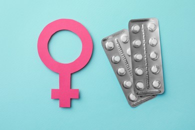 Photo of Female gender sign and blisters of pills on turquoise background, flat lay. Women's health concept