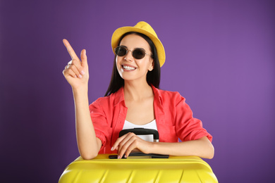 Beautiful woman with suitcase for summer trip on purple background. Vacation travel