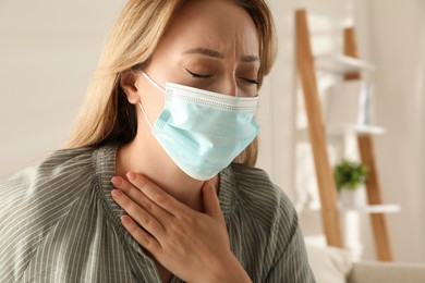 Photo of Young woman in medical mask suffering from pain during breathing indoors