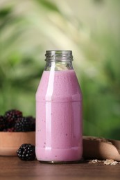 Delicious blackberry smoothie in glass bottle, oatmeal and berries on wooden table