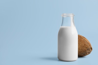 Photo of Glass bottle of delicious vegan milk and coconut on light blue background, space for text