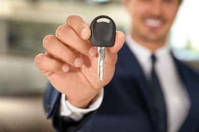 Young salesman with car key in modern dealership, focus on hand