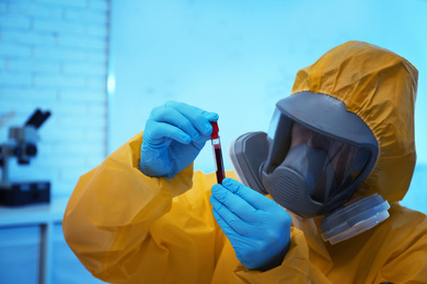 Scientist in chemical protective suit holding blood sample at laboratory, focus on test tube. Virus research