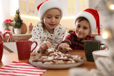 Cute little children taking tasty Christmas cookies from plate at  table in kitchen