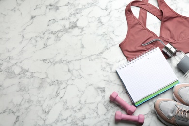 Flat lay composition with sportswear, notebook and dumbbells on white marble background, space for text. Gym workout plan