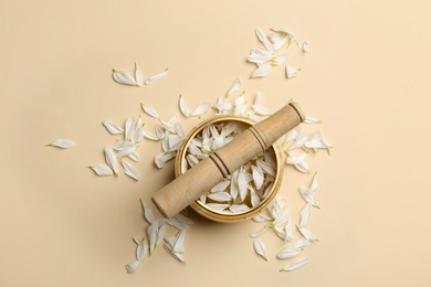 Golden singing bowl with petals and mallet on beige background, flat lay. Sound healing