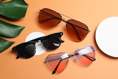 Photo of Different stylish sunglasses on pale orange background, flat lay