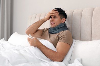 Sick man with scarf and tissue suffering from cold in bed at home