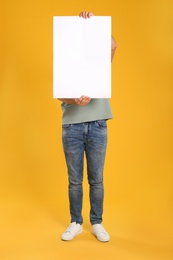 Man holding white blank poster on yellow background. Mockup for design