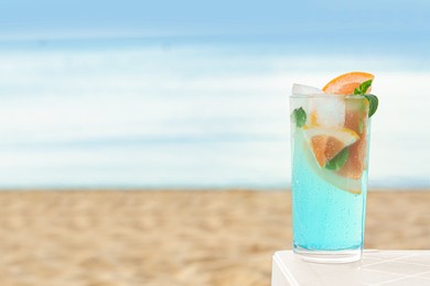 Photo of Glass of refreshing drink with grapefruit and mint on white table near sea, space for text