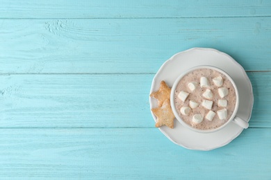 Delicious hot cocoa drink with marshmallows in cup and cookies on light blue wooden background, top view. Space for text
