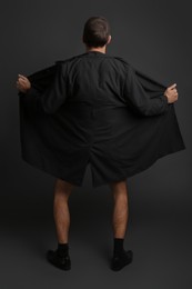 Exhibitionist exposing naked body under coat on black background, back view