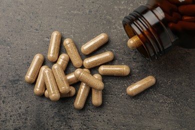 Overturned bottle with dietary supplement capsules on grey table, flat lay
