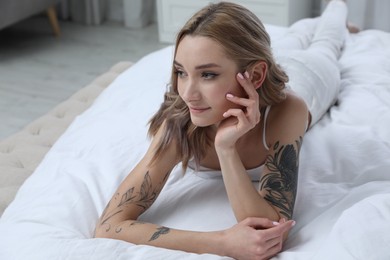 Photo of Beautiful woman with tattoos on body in bedroom