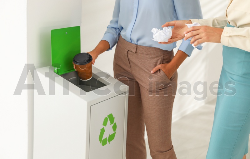 Young women throwing garbage into recycling bin in office, closeup