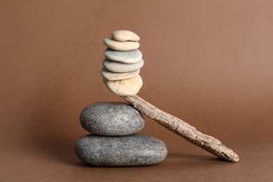 Stack of stones balancing on wooden stick against brown background. Harmony concept
