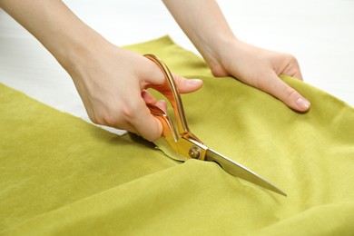 Photo of Seamstress cutting light green fabric with scissors at workplace, closeup