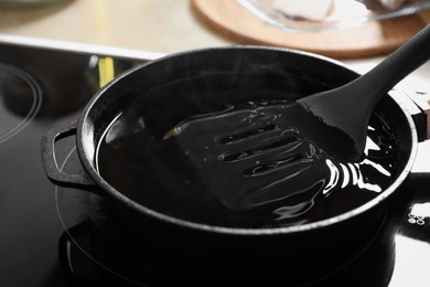 Photo of Frying pan with used cooking oil and spatula on stove, closeup