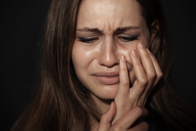 Crying young woman on dark background. Stop violence