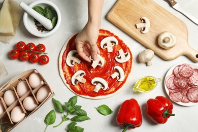 Woman putting mushrooms onto pizza crust with sauce on light table, top view