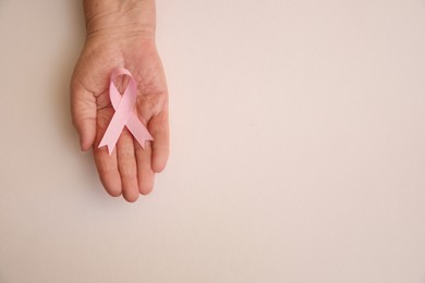 Photo of Senior woman holding pink ribbon on light background, top view with space for text. Breast cancer awareness