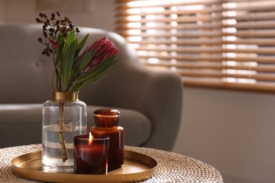 Photo of Vase with beautiful protea flower and candles on wicker stand indoors, space for text. Interior elements