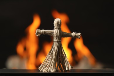 Photo of Voodoo doll on black table against blurred flame. Curse ceremony