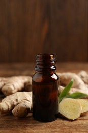 Glass bottle of essential oil and ginger root on wooden table