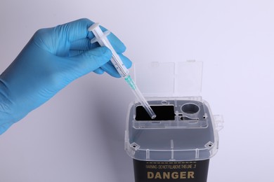 Doctor throwing used syringe into sharps container on white background, closeup