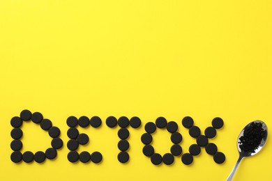 Photo of Word Detox made of activated charcoal pills and spoon on yellow background, flat lay with space for text. Potent sorbent