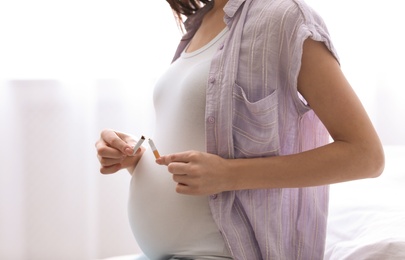 Young pregnant woman breaking cigarette at home, closeup