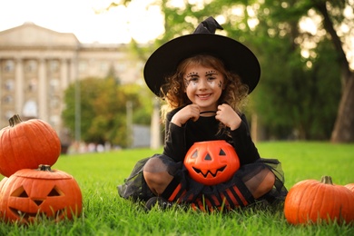Cute little girl with pumpkin candy bucket wearing Halloween costume in park