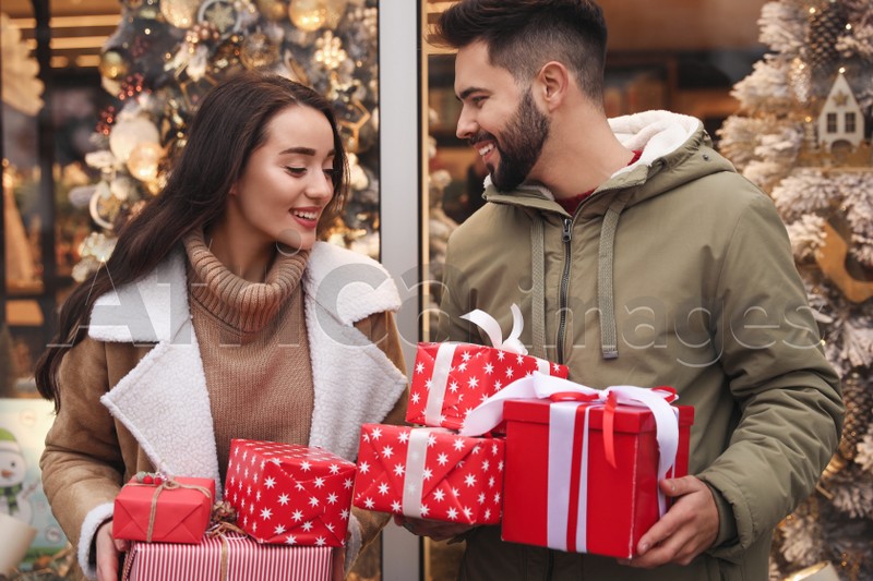 Lovely couple with presents near store decorated for Christmas outdoors