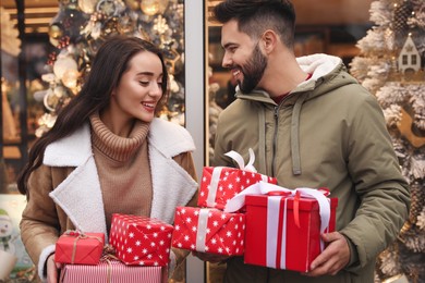 Lovely couple with presents near store decorated for Christmas outdoors