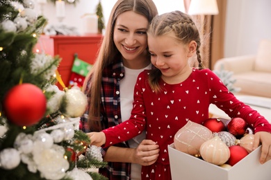 Happy mother with her cute daughter decorating Christmas tree together at home